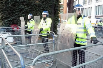 Police barriers form a strong barrier and three policeman stand behind of them.